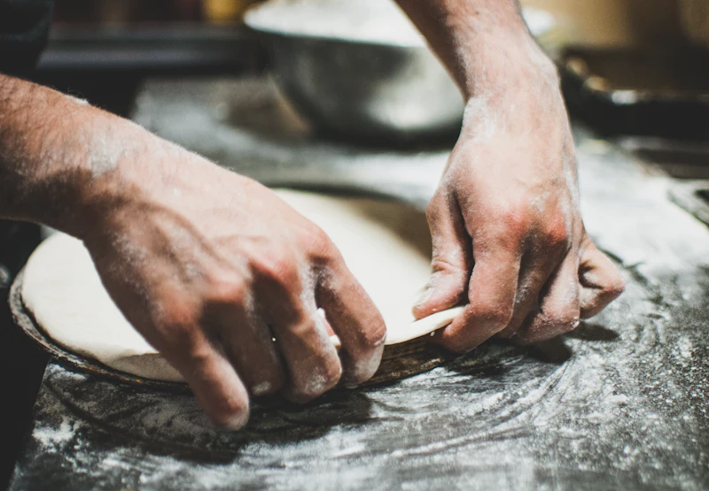 Mains qui étirent une pâte sur un plan fariné